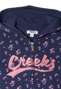Felpa con zip blu navy decorata con un motivo floreale rosa, con un logo "Creeks" rosa lucido. Tessuto morbido e cappuccio regolabile. Taglia 8 anni.