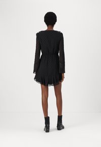 Vestido negro con cintura ajustada, mangas largas transparentes y un dobladillo acampanado, que presenta un patrón de lunares y acentos de volantes. Lleva botas de tobillo.