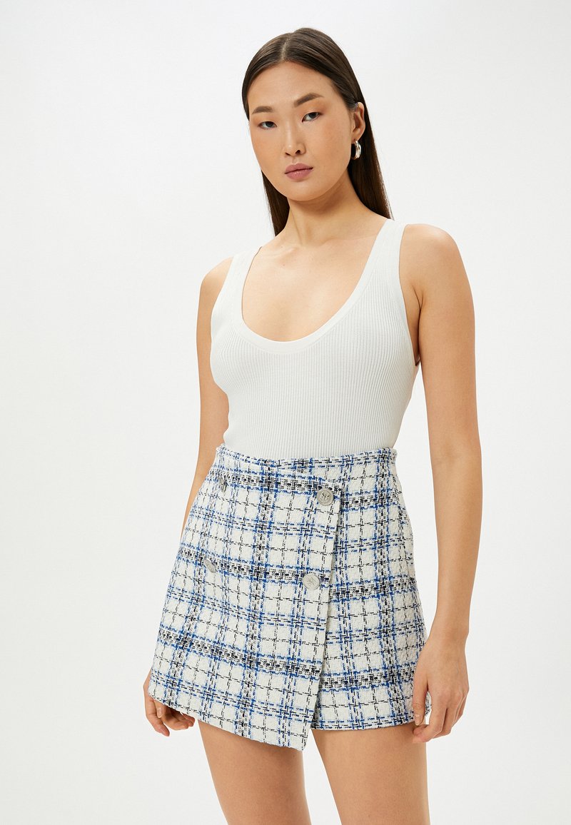 Witte geribde tanktop gecombineerd met een blauw-wit geruite minirok met knopen en gestructureerde stof. Eenvoudig en modern ontwerp.