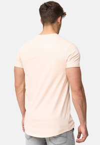 Pfirsichfarbenes T-Shirt mit kurzen Ärmeln und rundem Halsausschnitt, aus weicher Baumwolle, mit lockerer Passform und leicht verlängertem Rückensaum.