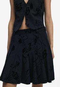 Gilet en tissu noir et jupe plissée avec un motif floral abstrait. Texture lisse, design ajusté avec des boutons et des poches latérales.