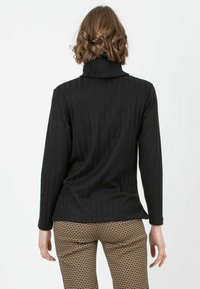 Schwarzer gerippter Rollkragenpullover mit langen Ärmeln, der einen hohen Kragen und eine lockere Passform aufweist. Strukturierter Stoff mit vertikalen Linien.