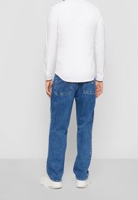 White long-sleeve button-up shirt paired with blue denim jeans, featuring a relaxed fit and back pockets, complemented by white sneakers.