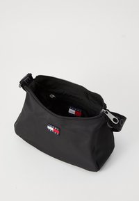 Musta nylon-pussi, jossa on vetoketjukiinnitys. Ominaisuuksia logo-patchi punaisena, valkoisena ja sinisenä. Pyöreä muoto ja tukeva kahva.