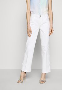 Jeans bianchi a gamba larga in jeans, con chiusura frontale a bottone, due tasche laterali e una texture liscia. Abbinati a un top leggero e trasparente.