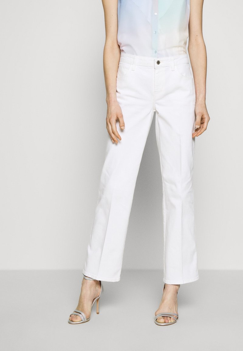 Jeans bianchi a gamba larga in jeans, con chiusura frontale a bottone, due tasche laterali e una texture liscia. Abbinati a un top leggero e trasparente.