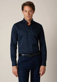 Granatowa koszula zapinana na guziki z subtelnym jasnym wzorem, długimi rękawami i klasycznym kołnierzem. Tkanina ma gładką fakturę i dopasowany krój.