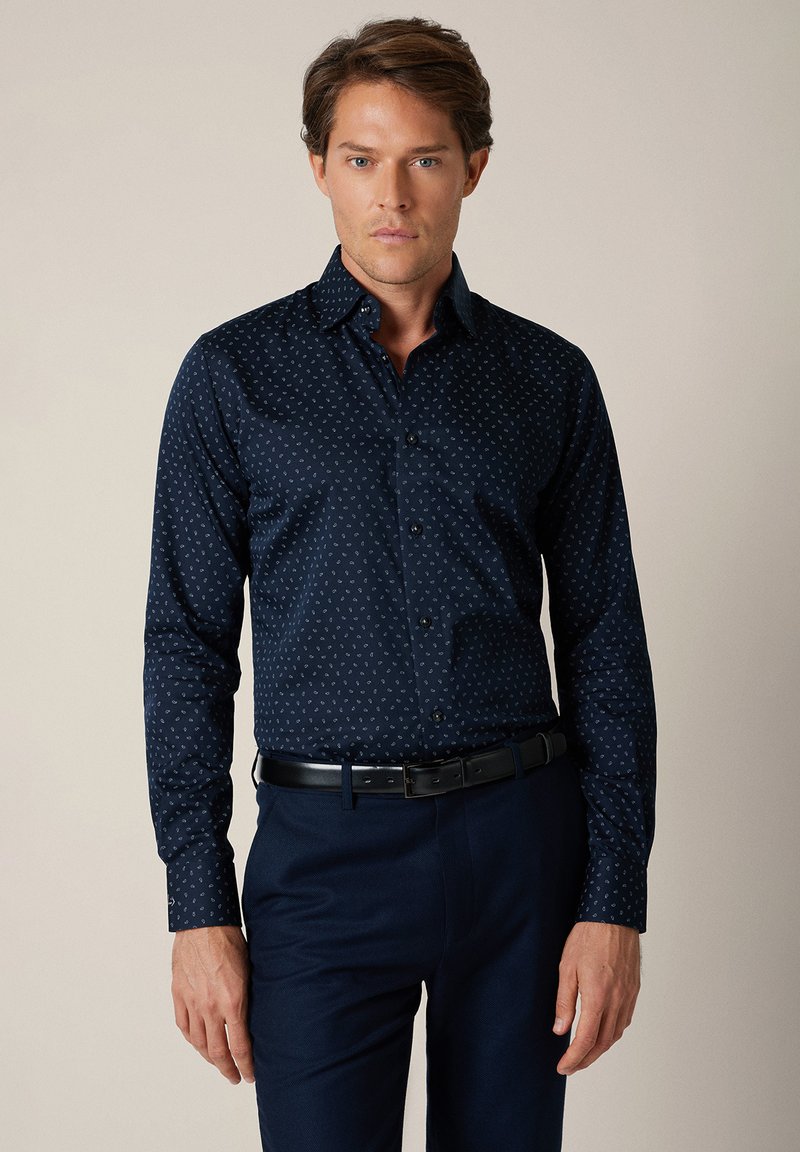 Granatowa koszula zapinana na guziki z subtelnym jasnym wzorem, długimi rękawami i klasycznym kołnierzem. Tkanina ma gładką fakturę i dopasowany krój.