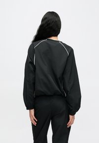 Fekete pulóver hosszú, ballon ujjakkal, rugalmas mandzsettákkal és fehér díszítéssel a varrások mentén. Könnyű anyagból, laza szabással.