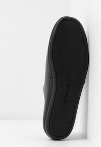 Čierne tenisky s hladkým koženým zvrškom, zaoblenou špičkou a štruktúrovanou gumovou podrážkou, s logom na spodnej strane.