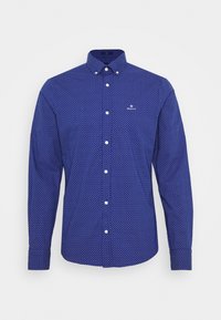 Camisa de manga larga en azul oscuro con un patrón geométrico, cuello abotonado y botones blancos. Presenta un pequeño logo en el pecho.