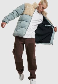 Padded jakna s kombinacijom svijetloplave i bež boje, s umjetnim krznom oko ovratnika i detaljem logotipa. Uparena s smešnim hlačama i patikama.
