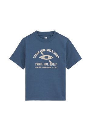 Blå t-shirt med korte ærmer med beige tekst "Cedar Fork River Camp" og "Paddle. Hike. Repeat." omkring en grafik af en kajak og en pagaj.