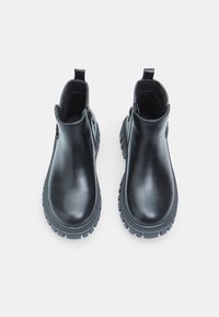 Botas de cuero negras hasta el tobillo con un acabado suave, suela de goma gruesa, cremalleras laterales y tiradores para facilitar su uso.
