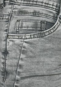 Close-up of faded gray denim jeans with visible stitching, rivet, and front pocket, highlighting fabric texture and button details.
