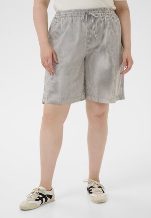 Person trägt kniehohe, grau-weiß vertikal gestreifte Shorts mit Kordelzug an der Taille und weiße Sneakers mit schwarzen Streifen.