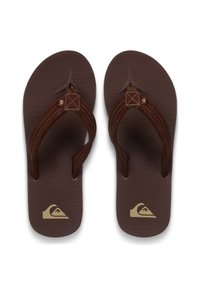 Καφέ σαγιονάρες με υφή στην επιφάνεια του πέλματος, καφέ υφασμάτινα λουριά και χρυσή λογότυπη λεπτομέρεια στη σόλα. Επίπεδο σχέδιο με λουριά τύπου σφήνας.