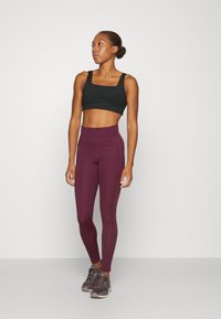 Fekete sportmelltartó, magas derekú bordó leggings, testhez simuló dizájn, sima textúra, szürke sportcipőkkel párosítva. Egyszerű, modern öltözet.