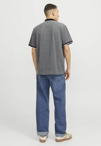 Pilkas polo marškinėlis su juodu apykakle, baltais rankovių krašteliais, derinamas su mėlynais džinsais ir smėlio spalvos sportbačiais, matomas iš nugaros.