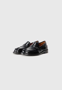 Par med svarte skinn penny loafers med brun innvendig fôr vist på hvit bakgrunn, vinklet til høyre.