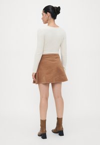 Langsleeve crème ribbeltop gecombineerd met een bruine ribcord A-lijn rok en bruine haklaarzen. Ronde hoepel oorbellen als detail.