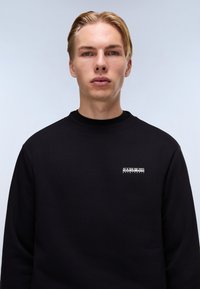 Sort crewneck sweatshirt lavet af bomuld, med et lille hvidt logo på brystet. Tykkere tekstur og ribbet kravedetalje.