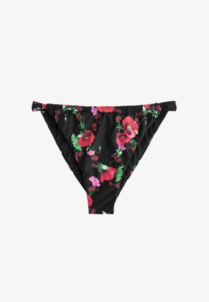 Close-up of a black floral fabric with red and pink flowers and a small metallic tag on gathered elastic waistband against tan skin.
