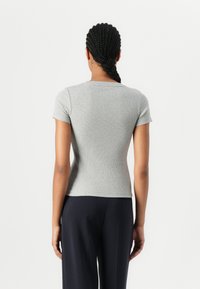 Top corto grigio a righe con collo rotondo, forma aderente e texture morbida, abbinato a pantaloni scuri, visto da dietro.