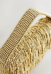 Goldfarbene Handtasche mit strukturiertem Oberflächen, ausgestattet mit einem dicken Tragegurt, der mit kleinen runden Perlen bedeckt ist und einen geschichteten Effekt erzeugt.