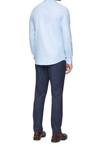 Helles blaues Langarmhemd kombiniert mit dunkelblauen Hosen und braunen Schnürschuhen, von hinten betrachtet, zeigt ein einfaches Design.
