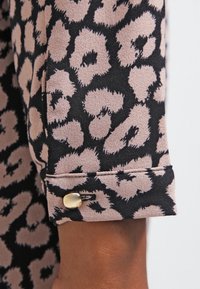 Leopard print fabric featuring black and beige colors. Cuffed sleeve with a gold button detail and smooth texture.