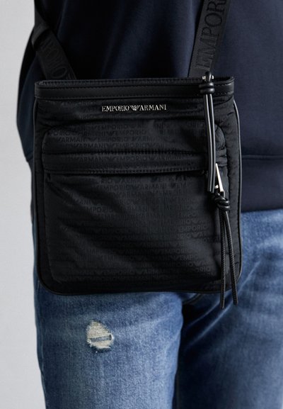 Geantă de umăr din material textile negru, cu logo Emporio Armani embosat, buzunare cu fermoar, curea ajustabilă și formă rectangulară elegantă.