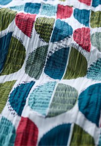 Multicolored cotton textile featuring large, circular patterns in blue, green, red, and white. Textured with varying line designs.