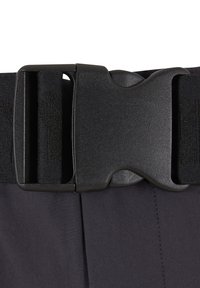 Close-up af en sort plastik hurtigudløser-spænde, der fastgør en sort justerbar vævet rem over mørkt stof.