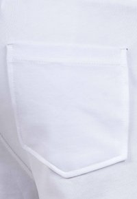 Witte stof met een gestructureerde afwerking, voorzien van een klein, rechthoekig patch pocket met contrasterende stiksels en afgeronde randen.