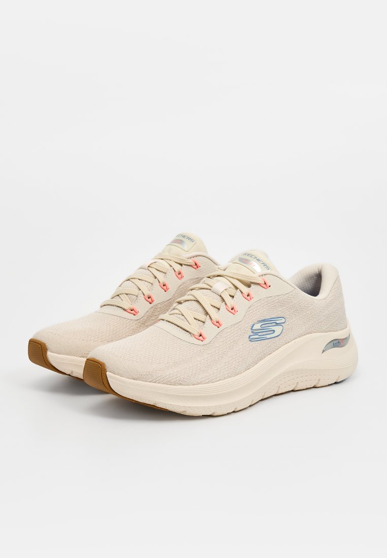 Zapatillas deportivas beige con una parte superior texturizada, detalles en rosa en los cordones y un logo azul claro. Presentan una suela acolchada y una forma redondeada.