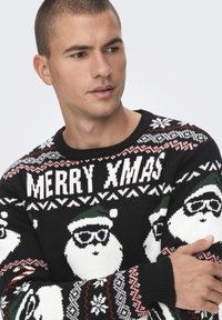 Svart strikkegenser med hvite Santa-ansikter med solbriller, røde og grønne detaljer, og "MERRY XMAS" i fet hvit skrift.