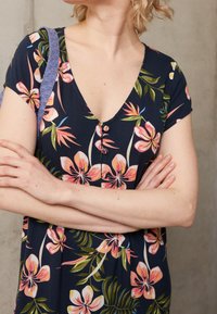 Robe bleu marine avec un motif floral tropical en rose et vert. Présente un décolleté en V profond et des boutons sur toute la longueur à l'avant. Tissu doux.