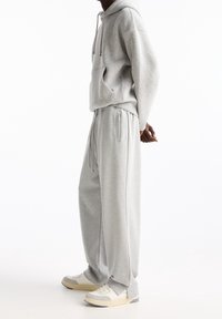 Grauer Kapuzenpullover mit Kängurutasche, kombiniert mit grauen Jogginghosen mit Kordelzug. Getragen mit weißen Turnschuhen.