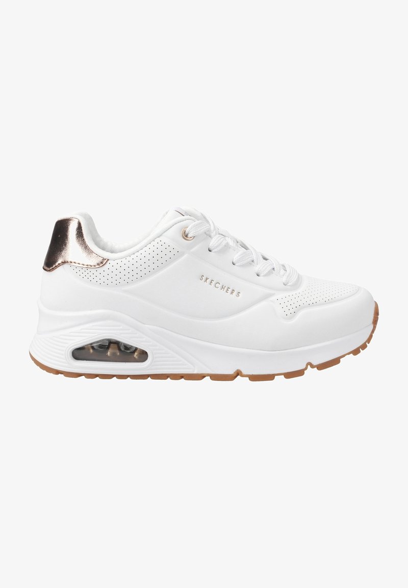 Baskets blanches Skechers avec un accent métallique or rose au talon, détails perforés, fermeture à lacets à l’avant et coussin d’air visible dans la semelle épaisse.