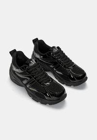 Pantofi sport negri, cu o combinație de materiale din plasă și lucios, formă rotundă, talpă groasă și sistem de închidere cu șireturi, prevăzuți cu un tab de prindere.