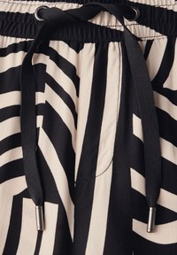 Black and cream patterned fabric with diagonal stripes, featuring an adjustable drawstring at the waist with metal aglets.