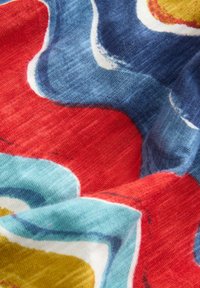 Gros plan sur un tissu doux avec des formes abstraites superposées en rouge, bleu, jaune et bleu clair, montrant la texture et les plis.