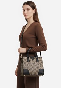 Borsa marrone e nera con corpo in tela a motivi, dettagli in pelle, doppi manici e tracolla rimovibile. Dettagli in metallo dorato.