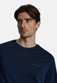 Granatowa, długosleeveowa koszulka z bawełny, z okrągłym dekoltem i subtelnym haftem logo na piersi. Gładka faktura.