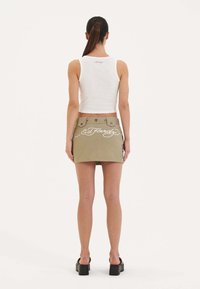 Bílý bezramínkový crop top v kombinaci s khaki mini sukní s vyšívanými grafikami a bílým písmem, nošený s černými platformovými botami.