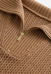 Brown knitted sweater featuring a zippered collar, ribbed texture, and open weave pattern. The zipper has a gold-tone finish.