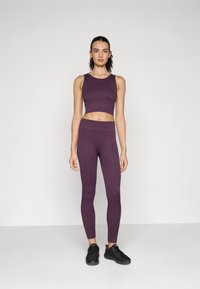 Lilla ribbet crop top og matchende leggings, der har et tætsiddende design og glat tekstur. Båret sammen med sorte træningssko.