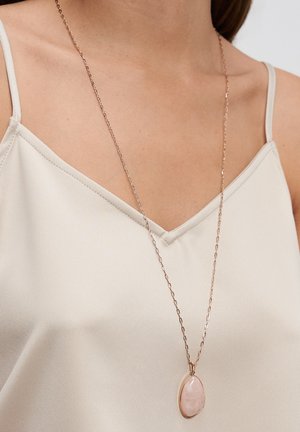 Halskette aus roségold mit einem tropfenförmigen Anhänger aus rosa Stein, getragen über einem hellbeigen Spaghettiträger-Top.