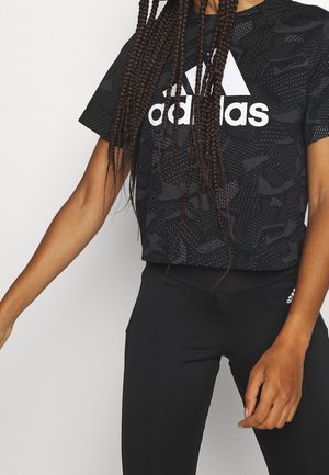 Femme portant un crop top noir Adidas et un legging noir avec le logo Adidas sur la cuisse, avec les cheveux longs tressés par-dessus le haut.